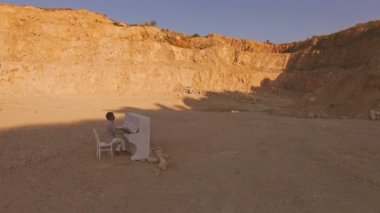 Genç adam dışarıda çıplak ayakla beyaz bir piyanoda çalıyor. Hava görüntüsü. Sürrealizm
