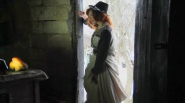 Etnik elbiseli güzel kızıl saçlı kız balkabağı almak için eski ahıra giriyor. Cadılar Bayramı.