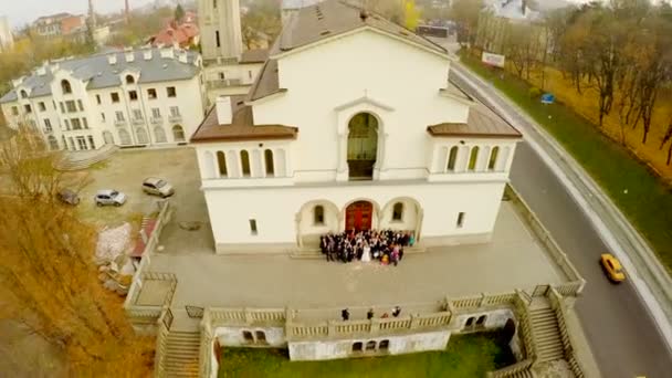 Letecký pohled na svatební obřad na ulici na prahu kostela na pozadí krásné podzimní krajiny. — Stock video
