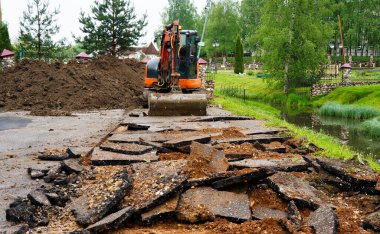 turuncu küçük kazıcı. Traktör kovasıyla asfalt kazın. Modern buldozer iş yerinde asfaltı ayırıyor