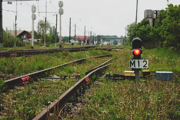 Red traffic light. Green natural railway background. On the right and on the left are the railway tracks, in the center the traffic light glows with a bright red light.