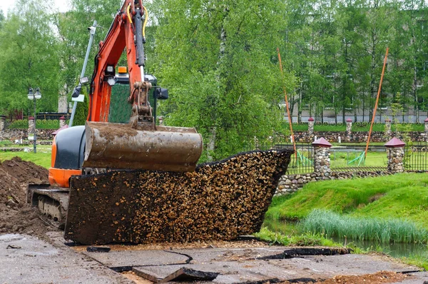 turuncu küçük kazıcı. Traktör kovasıyla asfalt kazın. Modern buldozer iş yerinde asfaltı ayırıyor