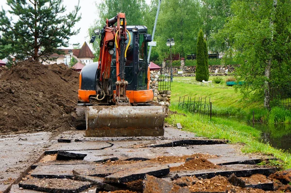 turuncu küçük kazıcı. Traktör kovasıyla asfalt kazın. Modern buldozer iş yerinde asfaltı ayırıyor