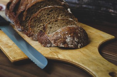 Tahtada dilimlenmiş çavdar ekmeği. Tahta bir masanın üzerinde ekmek için bir bıçakla