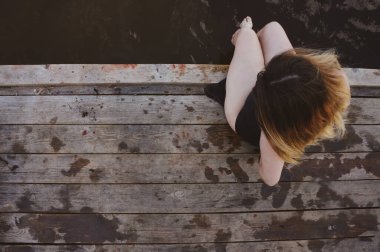  Mayolu tombul bir kız iskelede oturuyor ve suda ayaklarını tekmeliyor.