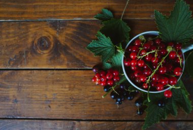 Beyaz fincanda kırmızı ve siyah üzümler ahşap bir arka planda, boşluğu kopyala