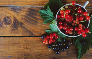 Beyaz fincanda kırmızı ve siyah üzümler ahşap bir arka planda, boşluğu kopyala