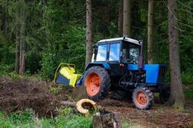 Ağaç kesiciler ve dallarla dolu bir traktör, orman arka planında odun öğütücü.