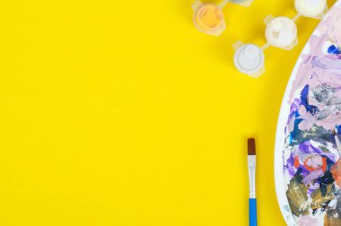 Akrilik boyalı kavanozlar ve sarı arka planda fırçası olan bir palet. Kopya alanı, yaratıcılık kavramı.