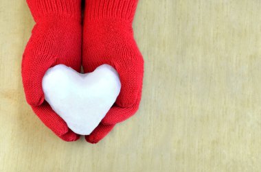 Tahta yüzeyde kırmızı eldivenli kar kalbi.