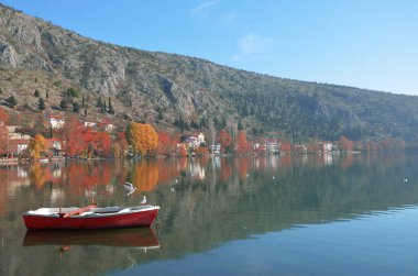 Kastoria gölündeki sonbahar yansımalarının güzel göl manzarası ve iki martılı bir tekne.