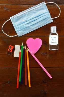 Okul malzemeleri Ağız maskesi ve ahşap masada sıvı el dezenfektanı.