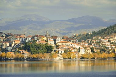 Amphiatral evler ve sarı yapraklı ağaçların olduğu sonbahar sahnesi Kastoria Gölü 'nün kıyısında.