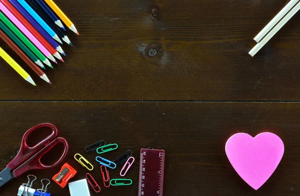 Colored pencils,pencils and  a heart shaped note sticker on wooden table