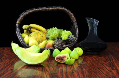 Sepetin üzerinde mevsimlik meyveler ve ahşap masada kırmızı şarapla sürahi.