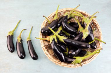 Tahta mavi bir masada sepetteki bebek patlıcanlar.