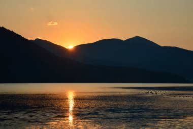 Altın saatinde göl sularına yansıyan dağ tepeleri ve güneş ışınlarının manzarası.
