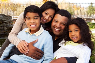 Biracial aile gülüyor ve dışarıda gülümseyen.