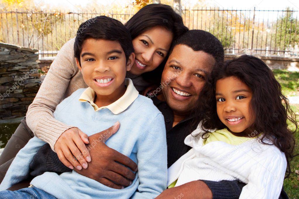 Biracial family laughing and smiling outside.