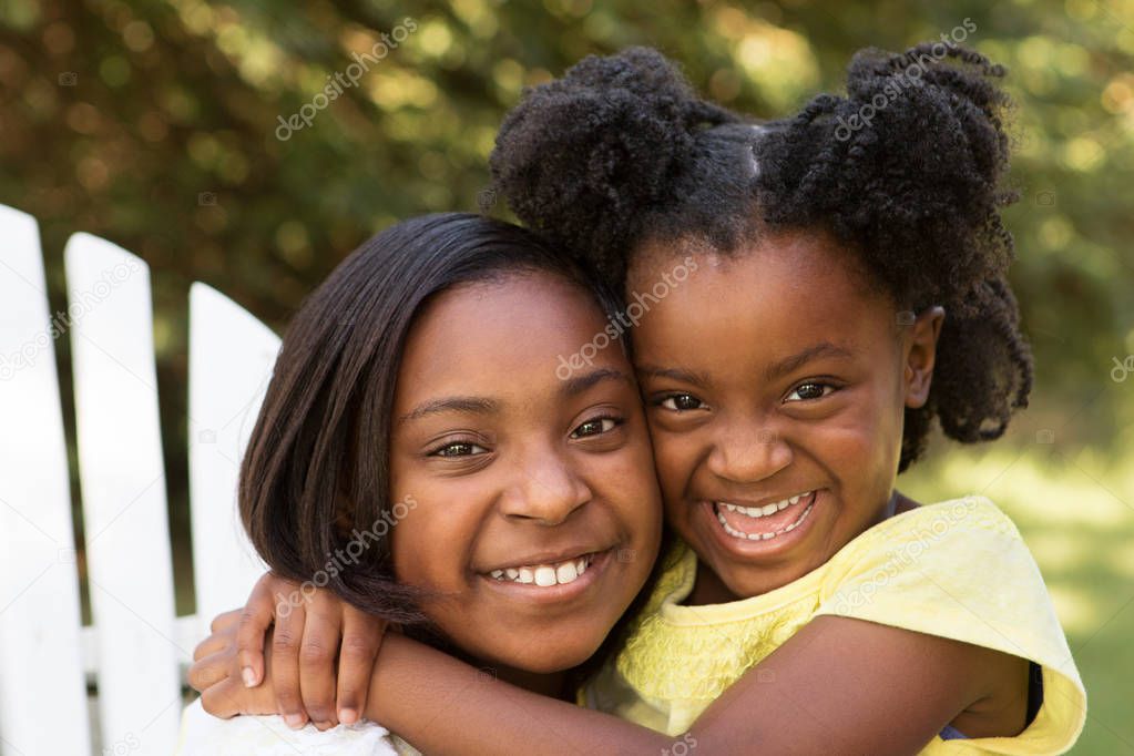 Portrait of two African American sisters hugging outside.