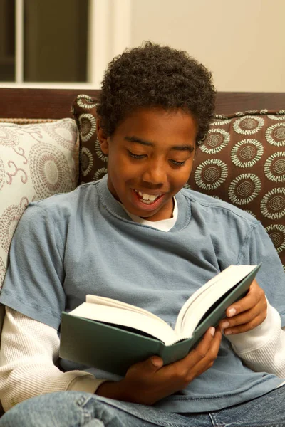 Junger afrikanischer amerikanischer Junge liest sitzend auf einem Sofa. — Stockfoto