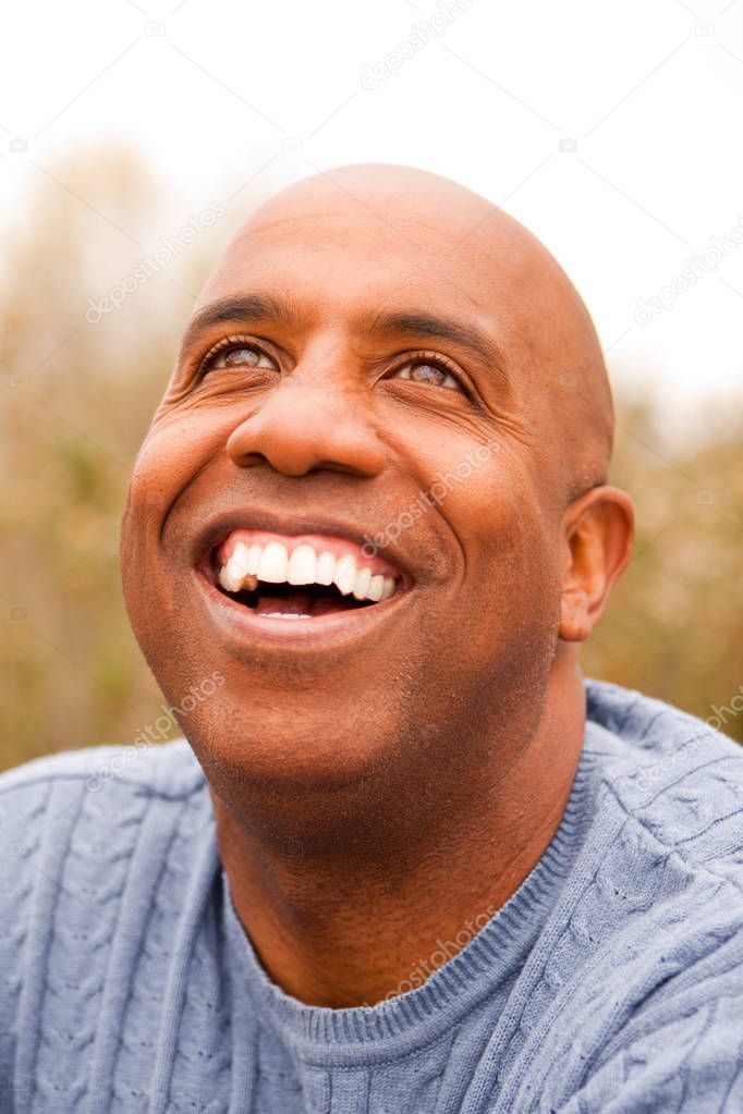 Mature African American man smiling sitting outside.