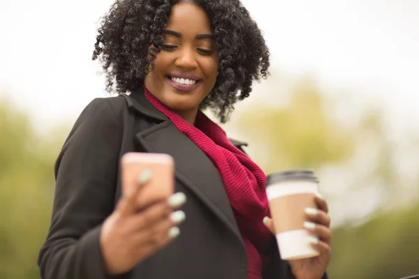 African American žena SMS a pití kávy. — Stock fotografie