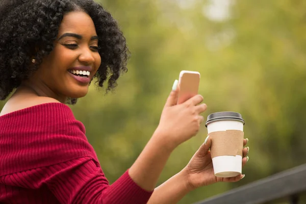 Mujer afroamericana mensajes de texto y beber café . — Foto de Stock