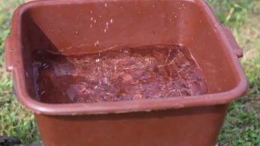 Elderly man with calloused and wounded hands washes away dirt with a bar of soap in a plastic basin on the street, his wife hands her husband a bar of soap,