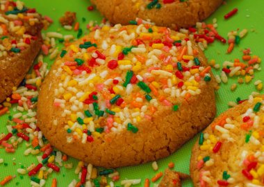 Yeşil bir masaya renkli şekerlemeler serpiştirilmiş vanilyalı kurabiyeler 