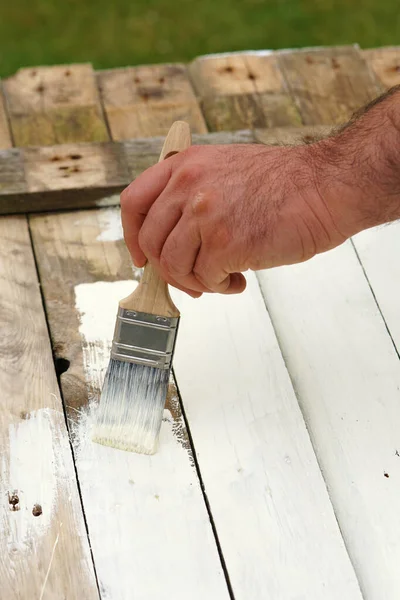 man paints old wood in white color