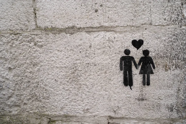 Ortasında kalp olan bir kadınla erkeğin el ele tutuştuğu sokak graffitisi. Duvarda bir çift.
