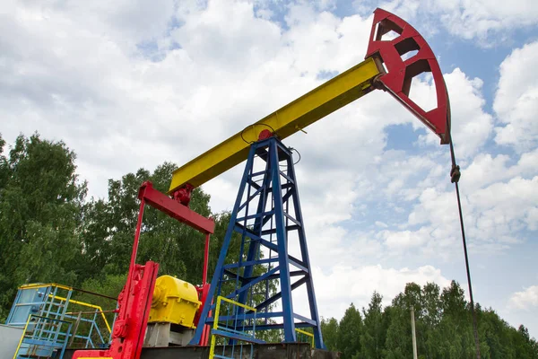 oil pumpjack against a cloudy sky stands among the tree