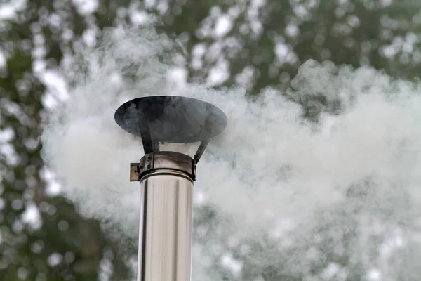 hot smoke escapes from a tin pipe against the background of autumn trees