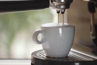 Beyaz bir fincanda kahve makinesiyle kapuçino yapmak.