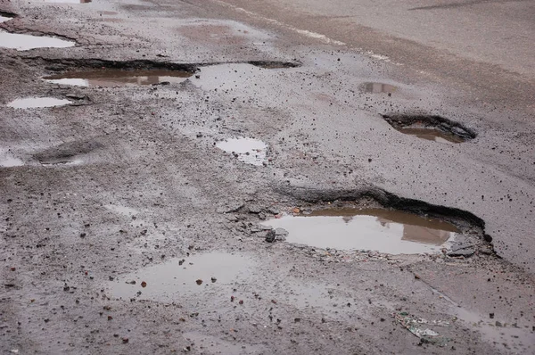 冬の壊れたアスファルト道路 水と多くのピット — ストック写真