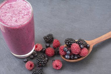 Ahududu, böğürtlen ve yaban mersini dağılım bir tahta kaşık ve smoothies bu uzuvlar siyah bir zemin üzerine bir sürü.