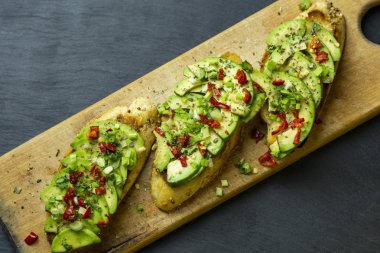 Avokado dilimleri, yeşil soğan, baharat ve biber siyah bir arka plan karşı bir ahşap tepsi ile üç bruschetta.