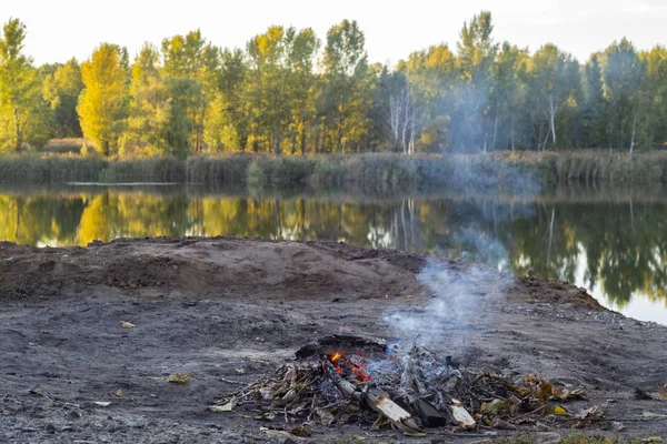 A small fire is burning on the shore of a beautiful lake.