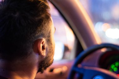 Akşam bir adam bir arabanın direksiyonuna oturuyor - arka görüş.