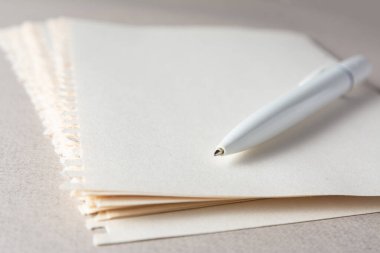 Beyaz bir kalem, soyut bir bej arka plandaki bir defterden yırtılan hafif kağıtların üzerinde yatar..