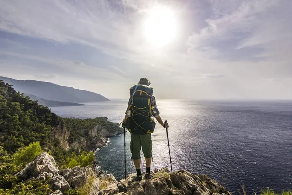 Tourist with backpack standing on a cliff in mountains near mediterranean sea — Stock Photo, Image