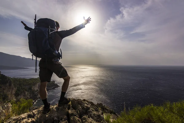 Tourist with backpack standing on a cliff in mountains near mediterranean sea — Stock Photo, Image