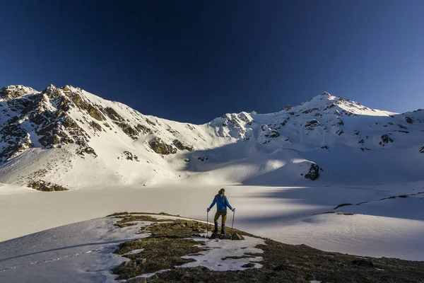 Homem de pé em um penhasco em montanhas nevadas ao pôr do sol — Fotografia de Stock