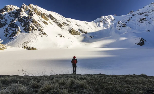 Homem de pé em um penhasco em montanhas nevadas ao pôr do sol — Fotografia de Stock