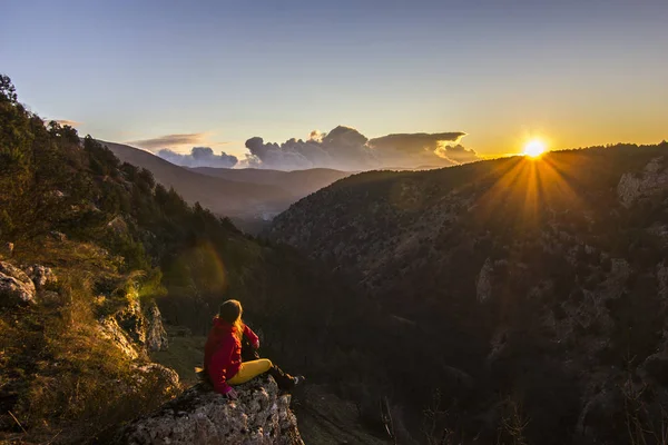 Fille assise sur une falaise dans les montagnes au coucher du soleil — Photo