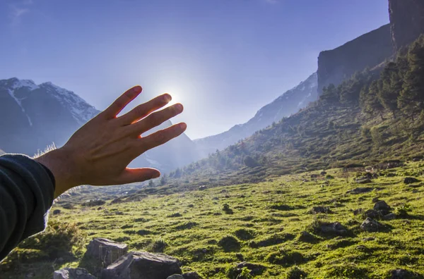 Mão de homem cobre sol em montanhas com campos de grama verde — Fotografia de Stock