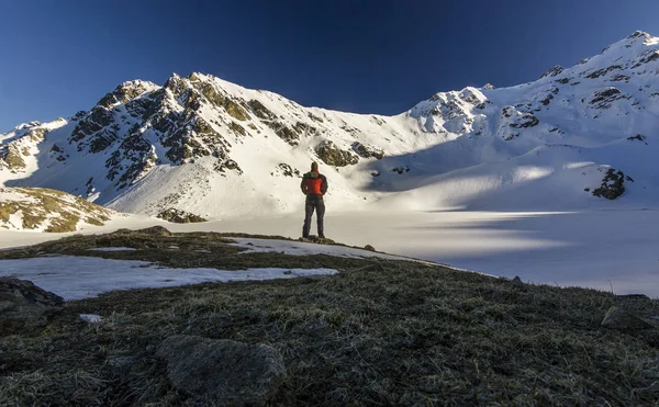 Homem de pé em um penhasco em montanhas nevadas ao pôr do sol — Fotografia de Stock