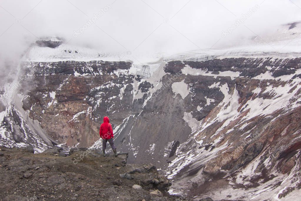 man standing on Tolbachik volcano crater with snow on hills