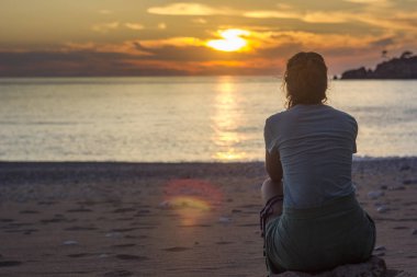 girl sitting on sandy beach near mediterranean sea at sunset clipart